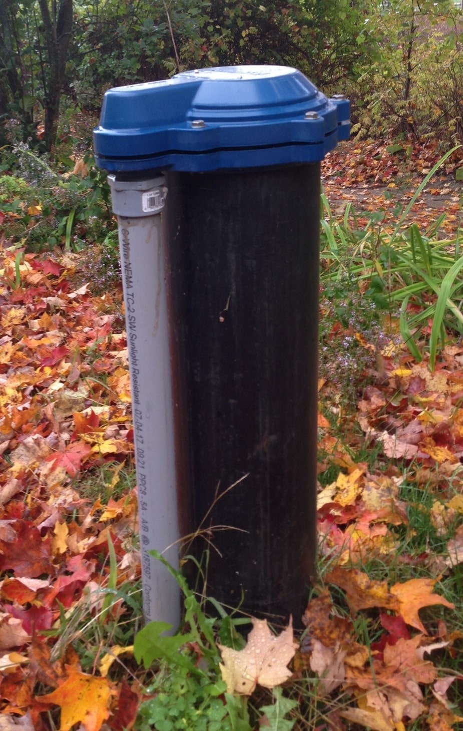 Example well casing with a blue cap and exterior grey electrical conduit; buried pitless connection is not visible